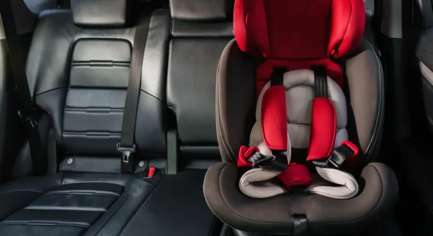 Czerwony fotelik dziecięcy z pasami bezpieczeństwa zamontowany w samochodzie. System isofix w samochodzie zapewnia bezpieczne podróżowanie najmłodszych.