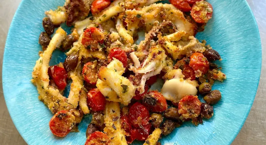 Calamari gratinati al forno su piatto blu, con pomodorini e olive.