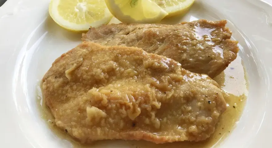 Deliziose scaloppine al limone, succulente e dorate, servite con spicchi di limone fresco.