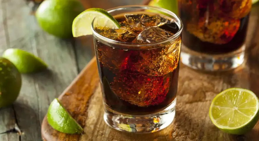 Orzeźwiający drink: bacardi z czymś ciemnym i lodem, ozdobiony plasterkami limonki.