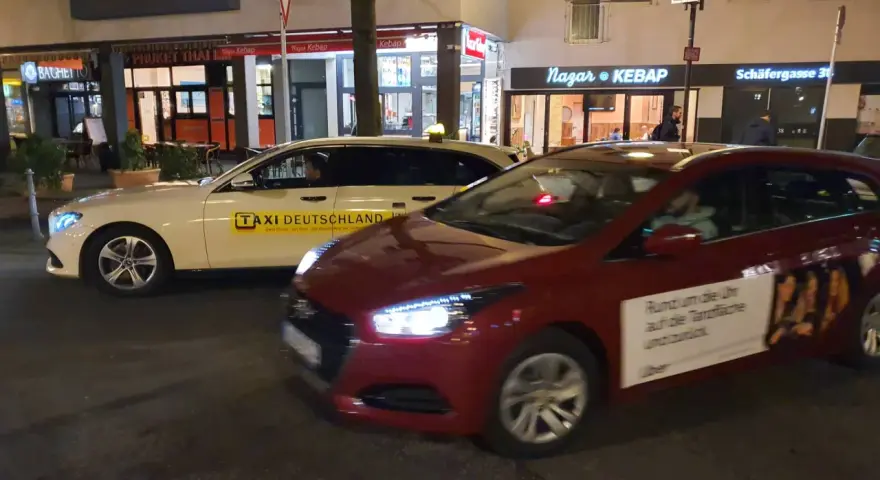 Ein weißes Taxi und ein rotes Auto mit Uber-Werbung stehen nebeneinander. Der Unterschied über Taxi ist die moderne Alternative.