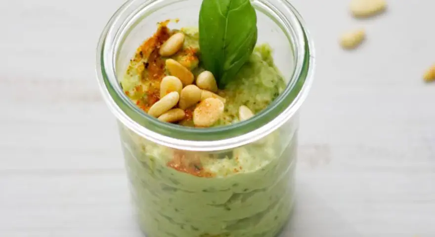 Cremiges Avocado Pesto in einem Glas, garniert mit Pinienkernen, Basilikum und Paprikapulver. Ein Genuss für jeden Tag!