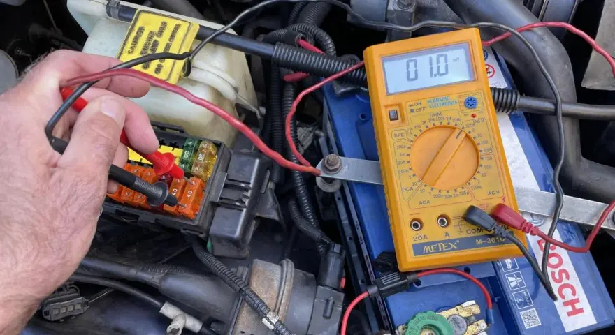 Testing for a parasitic draw with a multimeter connected to the car battery. A reading of 01.0 mV indicates a small current drain.