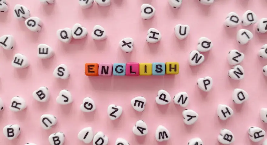 Kolorowe koraliki z literami tworzą napis "ENGLISH" na różowym tle.
