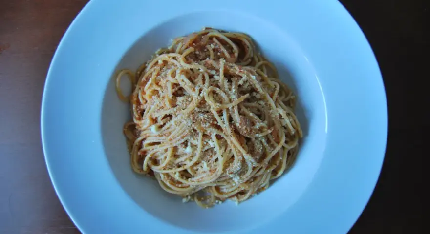 Spaghetti Napoli z sosem pomidorowym i parmezanem, podane w białej głębokiej misce.