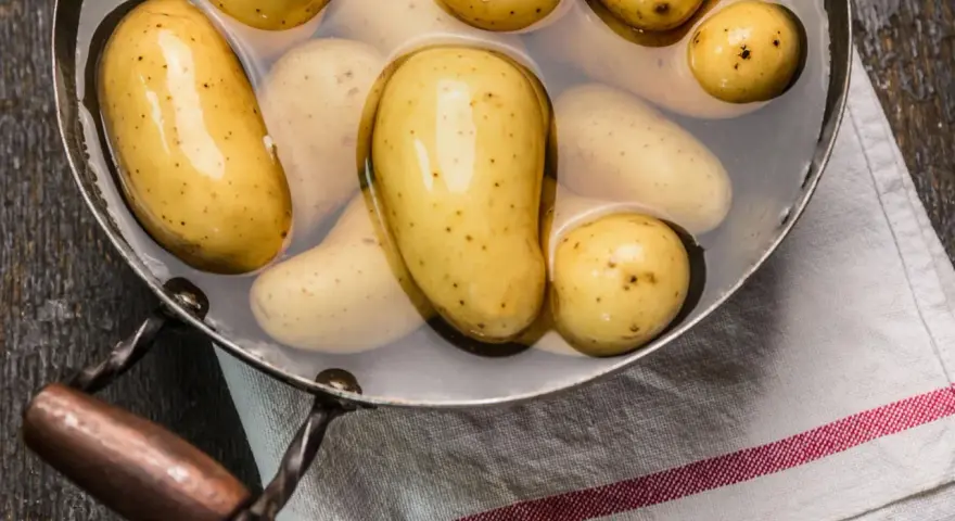 Kleine, gelbe Kartoffeln liegen in Wasser in einem Topf. Sie sind bereit, um sie zu kochen.