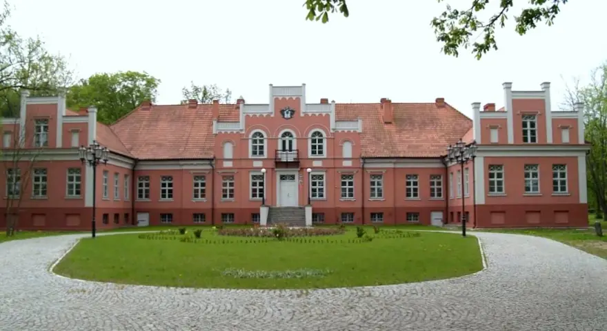 Pałac Przebendowskich w Wejherowie, różowy, z czerwonym dachem, otoczony zielenią i brukowanymi alejkami.