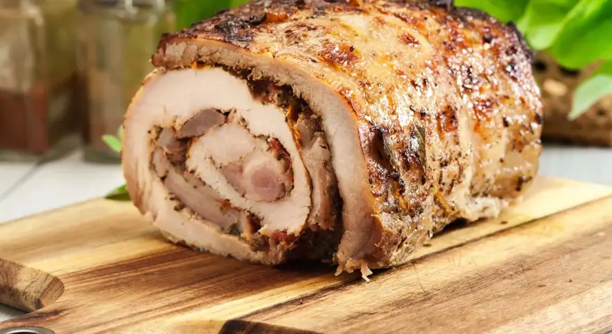 Redondo de ternera relleno, dorado y jugoso, sobre tabla de madera.