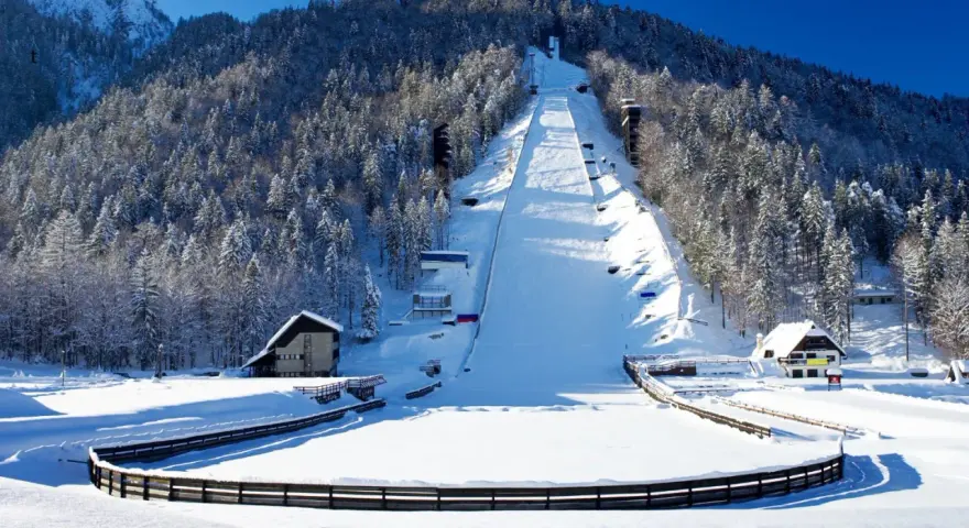Zimowa Planica w Alpach Julijskich, z ośnieżoną skocznią narciarską i lasem iglastym.
