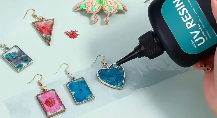 A hand applies UV resin to a heart-shaped earring with blue flowers, demonstrating how UV resin works to create beautiful jewelry.