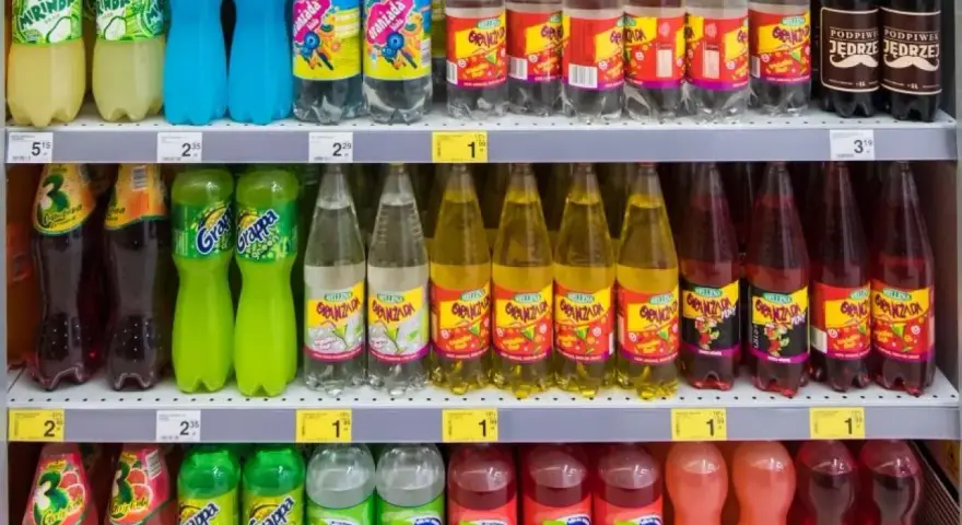 Półki sklepowe z różnymi napojami gazowanymi w plastikowych butelkach.