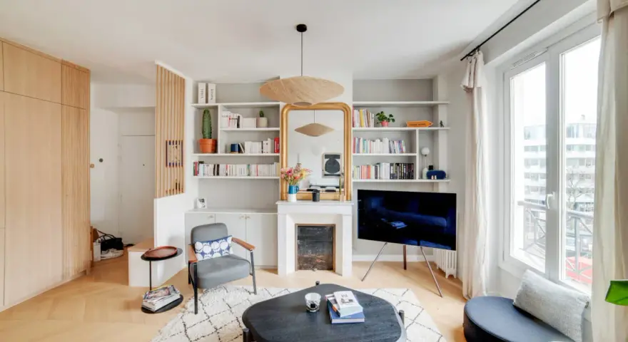 Aménagement entrée ouverte avec rangements boisés, fauteuil, cheminée décorative et étagères remplies de livres.