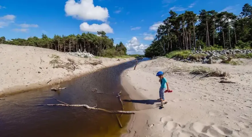 Dziecko w kasku spaceruje po piaszczystej plaży nad jeziorem Kopań. Atrakcje przyrodnicze i spokój.