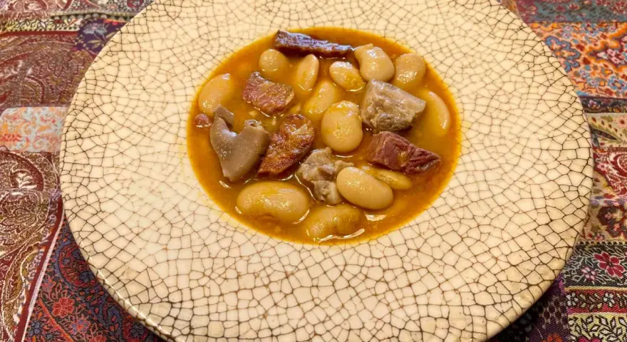 Plato de judiones de la granja receta tradicional, con trozos de tocino y carne en un caldo sabroso.