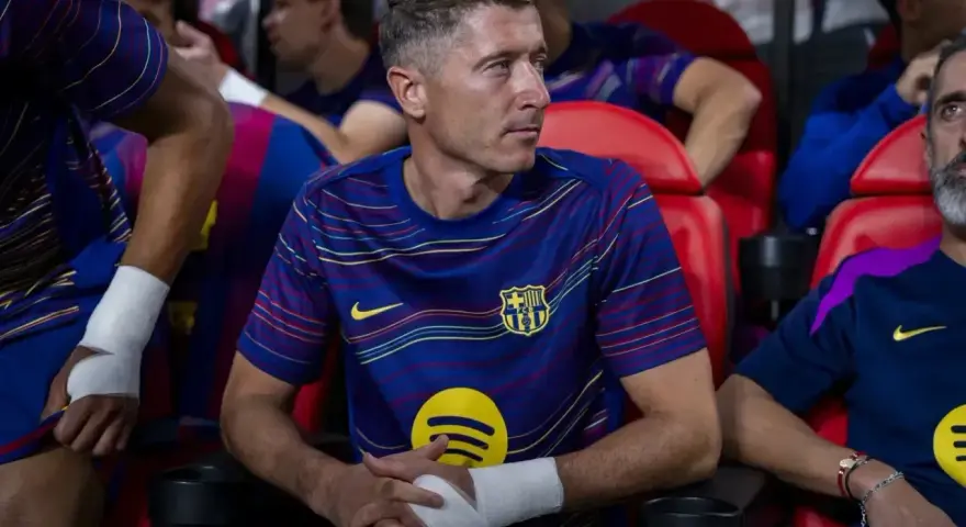 Robert Lewandowski w meczu FC Barcelona – Valencia CF, siedzi na ławce z bandażem na ręce, skupiony na grze.