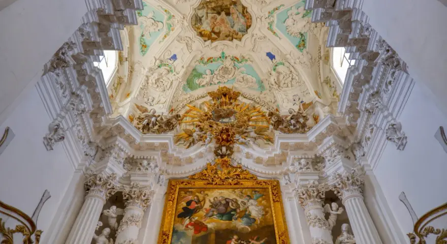 Magnifique plafond orné de fresques et de sculptures, typique du style baroque, avec un tableau doré au centre.