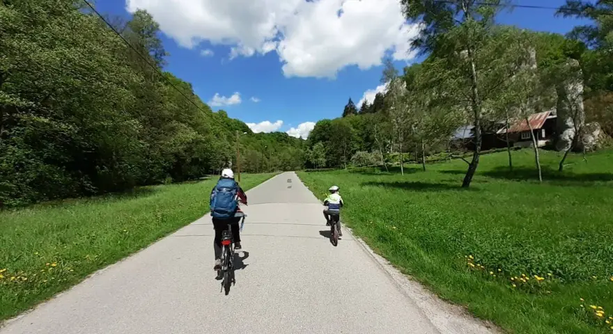 Dwie osoby na rowerach przemierzają malownicze **ojcowskie park narodowy trasy rowerowe**. Słoneczny dzień, zieleń i chmury na niebie.