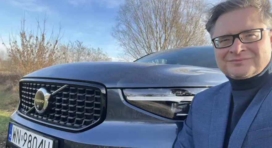 Mężczyzna w okularach i garniturze pozuje do zdjęcia z przodu Volvo XC40. Czy są jakieś wady tego modelu?