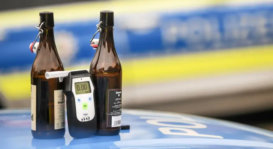 Zwei Bierflaschen und ein Alkoholtester auf einem Polizeiauto. Der Tester zeigt 0.00, aber die Gefahr einer 1 1 Promille Strafe bleibt.