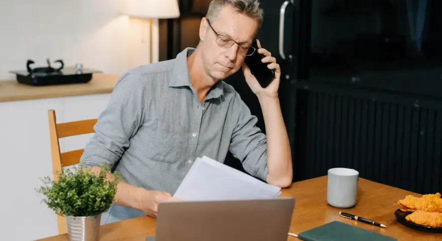 Mann am Telefon, der Dokumente prüft. Frustriert, weil die Kfz-Versicherung nicht zahlt.
