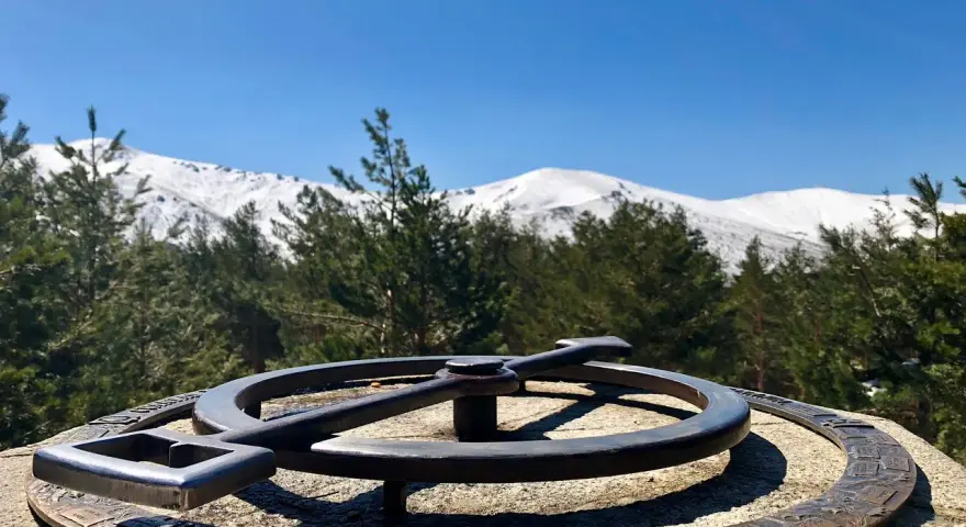 Un mirador de la gitana con un compás de bronce y montañas nevadas al fondo.
