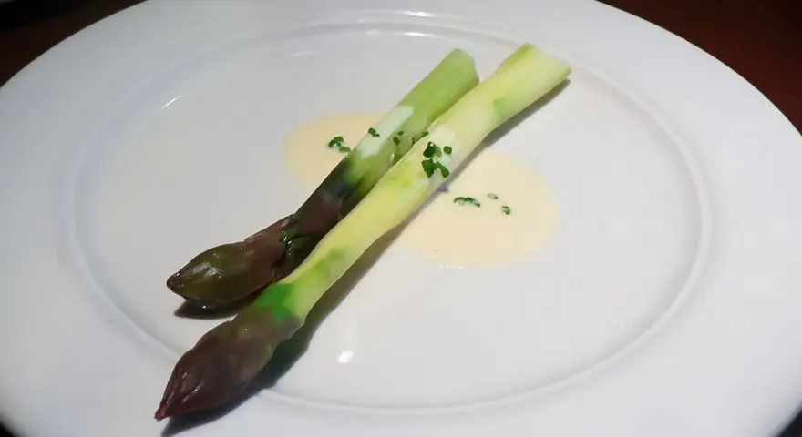 Zwei Spargelstangen auf einem Teller, serviert mit einer cremigen beurre blanc Sauce und gehackten Kräutern.