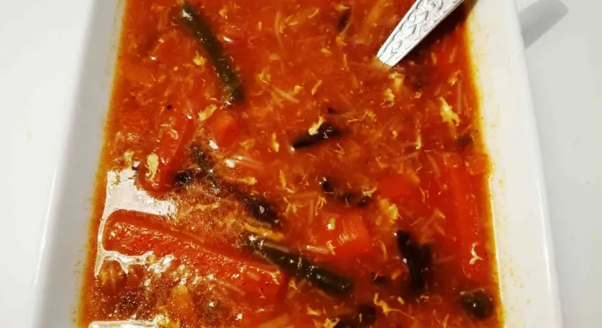 Aksamitna zupa ostro kwaśna z kawałkami warzyw i jajka, podana w białej misce.