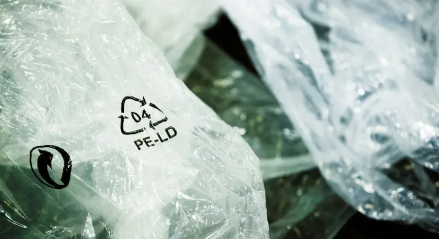 Zgniecione folie PE-LD z symbolem recyklingu. Firma stawia na recykling tworzyw sztucznych, dbając o środowisko.