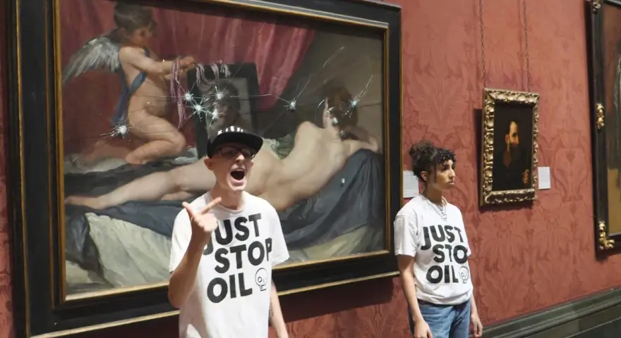 Dwie osoby w koszulkach "Just Stop Oil" stoją przed obrazem "Wenus z lustrem", który został uszkodzony.