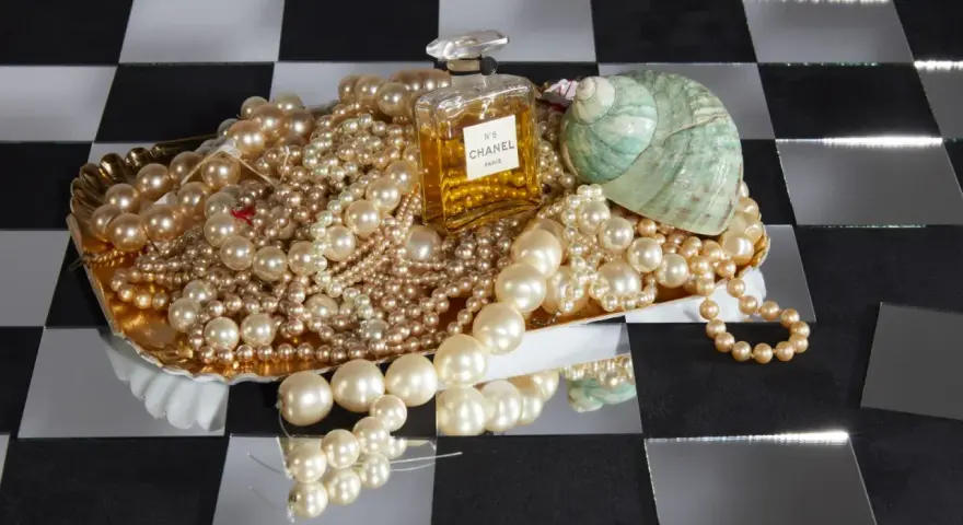 Perle, profumo Chanel N°5 e una conchiglia su un vassoio dorato. Il profumo evoca il **chanel significato** di lusso e raffinatezza.