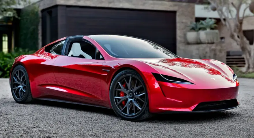 Błyszczący, czerwony Tesla Roadster 2 z białymi siedzeniami stoi przed nowoczesnym domem.