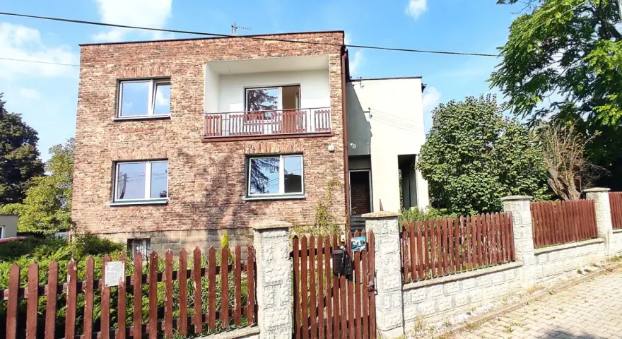 Nowoczesna metamorfoza domu z lat 80. z ceglaną fasadą, balkonem i drewnianym płotem.