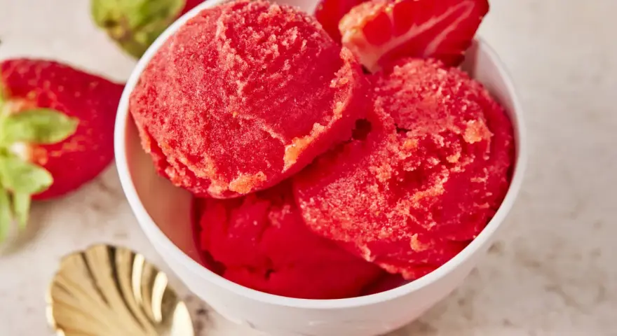 Schüssel mit erfrischendem Erdbeer Sorbet, garniert mit frischen Erdbeeren und einer goldenen Löffel.