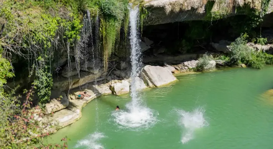 Disfrutando del baño en piscinas naturales junto a la cascada de Tobera. Un grupo de amigos se lanza al agua turquesa.