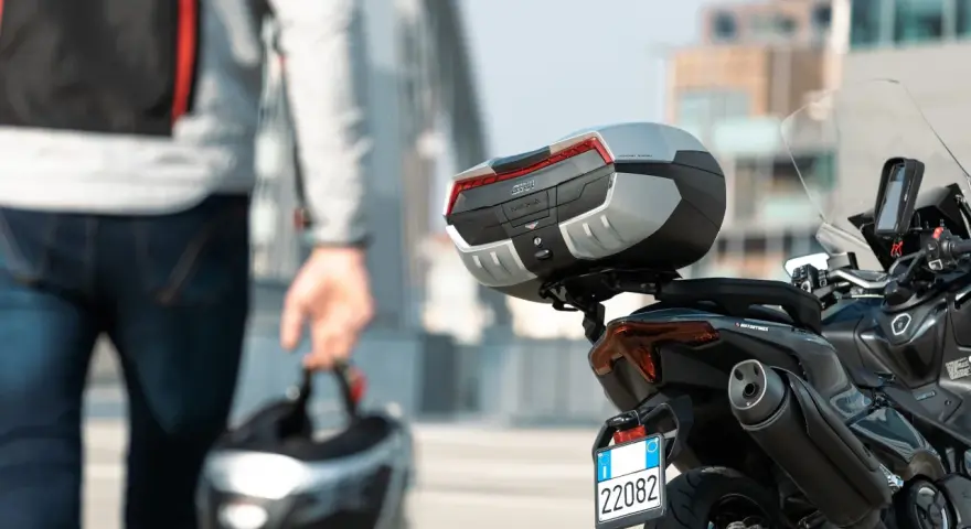 Un motociclista con casco in mano si avvicina alla sua moto. Andare in moto fa bene, un'avventura ti aspetta!