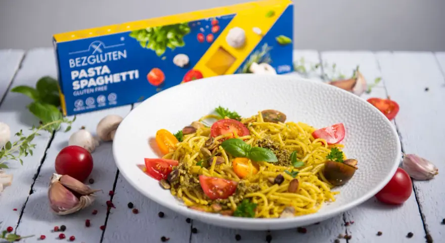 Pyszny talerz makaronu spaghetti bezglutenowego z pesto, pomidorkami i migdałami. Obok pudełko makaronu.