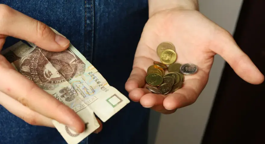 Dłoń trzyma banknot 20 zł i garść monet. Symbolizuje to spłatę długu po wyroku sądowym, gdzie każda złotówka ma znaczenie.