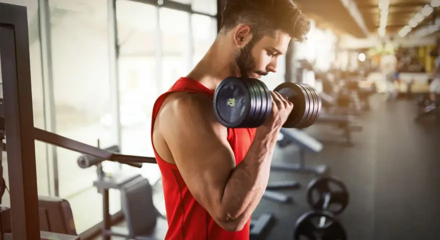 Hombre con barba entrenando bíceps con mancuerna en gimnasio. ¿Cuál es la mejor hora para entrenar?