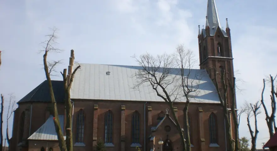 Sanktuarium w Swarzewie, ceglany kościół z wysoką wieżą, otoczony drzewami o nagich gałęziach.