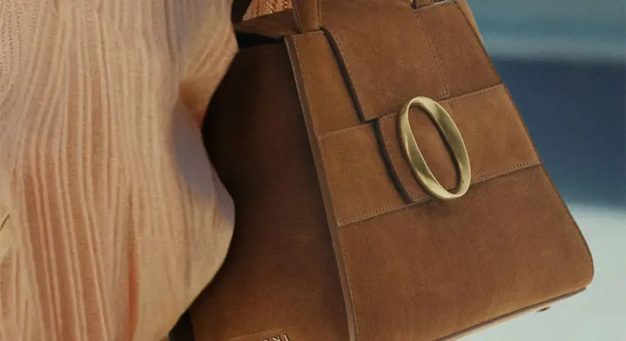 Borsa in camoscio marrone con fibbia dorata. La texture morbida evidenzia la differenza tra camoscio e pelle scamosciata.