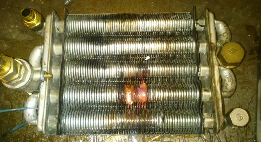 Scambiatore caldaia con evidenti segni di bruciatura, causa rottura scambiatore caldaia. Componenti metallici corrosi e deformati.