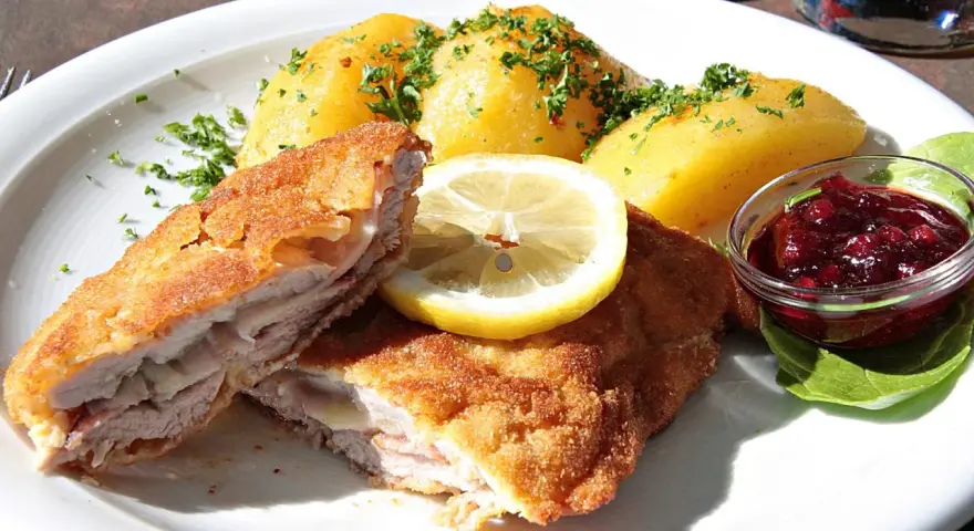 Kotlet po szwajcarsku z ziemniakami, cytryną i żurawiną. Pyszne danie na talerzu.