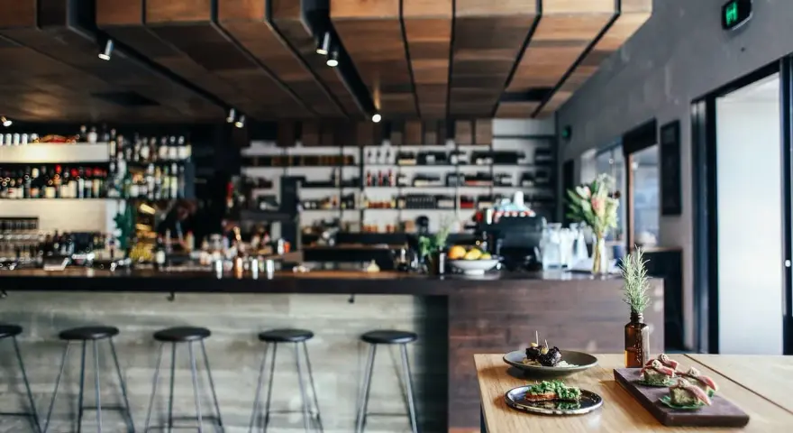 Ambiente restaurante moderno con barra, taburetes y aperitivos en mesa.