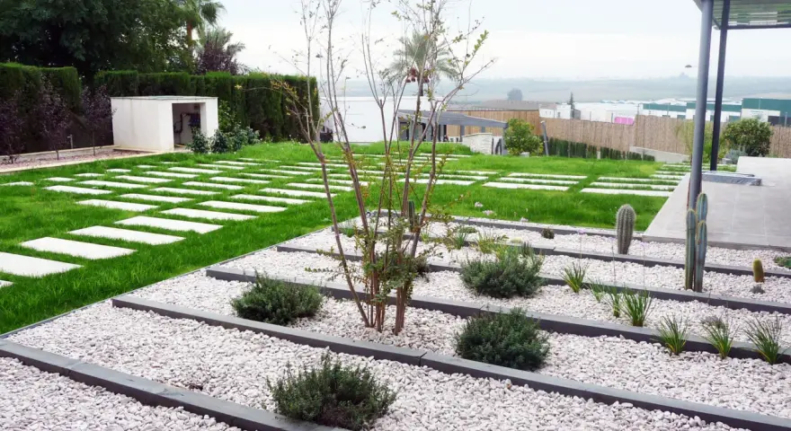 Vialetti giardino moderni con lastre quadrate su prato verde e aiuole di ghiaia bianca con piante succulente e arbusti.
