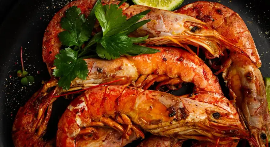 Gambones a la plancha, jugosos y dorados, servidos con perejil fresco y rodajas de lima. ¡Un manjar irresistible!