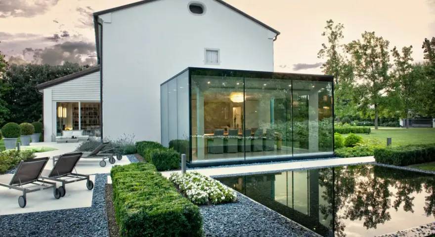 Ampliamento casa con estensione esterna in vetro, con piscina e arredi da giardino.