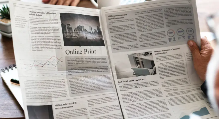 Manos sostienen un periódico con artículos sobre marketing y finanzas, impreso en gramaje papel normal.