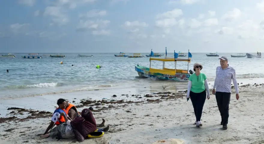 Spacerowery na plaży w Somalii, z łodziami na morzu. Czy Somalia jest bezpieczna? Turyści spacerują, podczas gdy lokalni mieszkańcy odpoczywają na piasku.