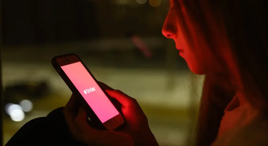 Dziewczyna patrzy na ekran telefonu z logo Tindera. Zastanawia się, co odpisać na "czego szukasz na Tinderze?".