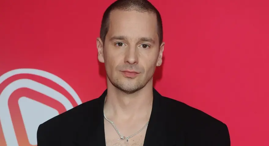 Krzysztof Zalewski w czarnym garniturze, z naszyjnikiem, na tle czerwonym z białym logo.